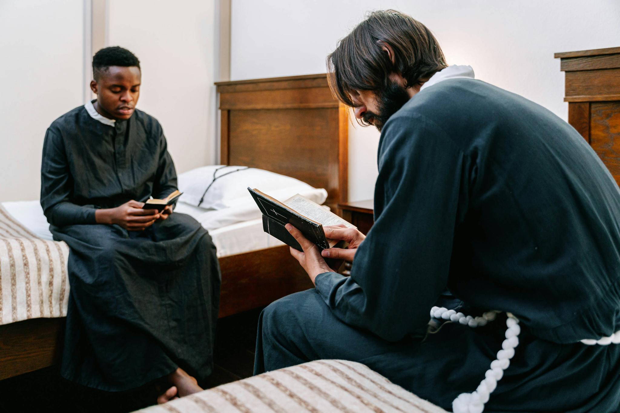 Two seminarians praying and studying the Bible in a dorm room, wearing robes.
