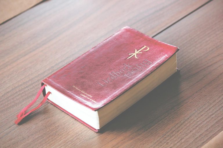 A red vintage-style Bible with ornate design lies on a wooden table, symbolizing knowledge and spirituality.